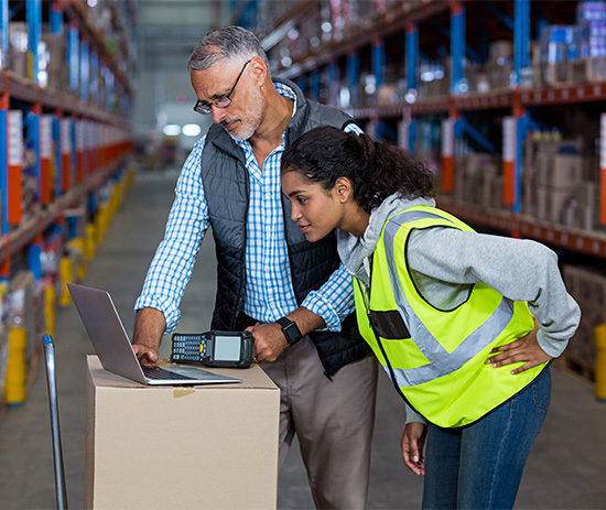 older and younger warehouse workers looking at a laptop