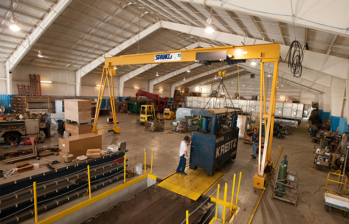 man using a gantry crane to move a large, heavy component in a manufacturing facility