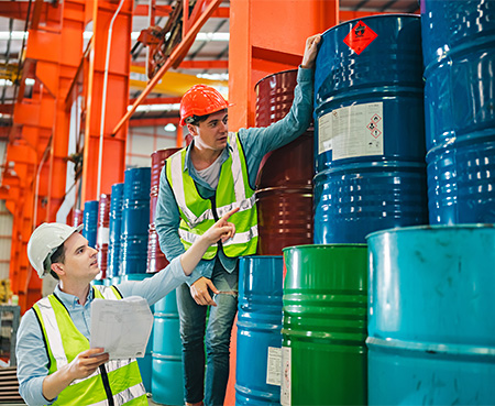 workers pointing to drums labeled as hazardous