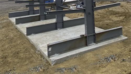 Pouring a rated concrete slab to support an outdoor installation is one way to increase stability and safety. This picture shows a poured base for a cantilever rack system on a dirt area.