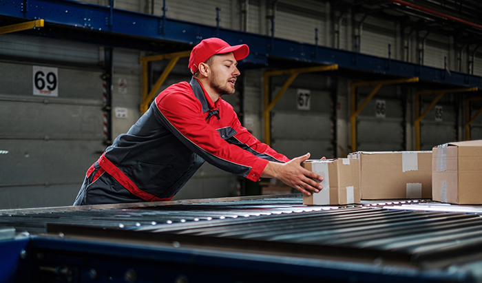 Worker at a distribution center reaching over a conveyor to retrieve a package.