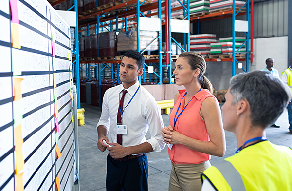 warehouse workers looking at sticky notes on a board